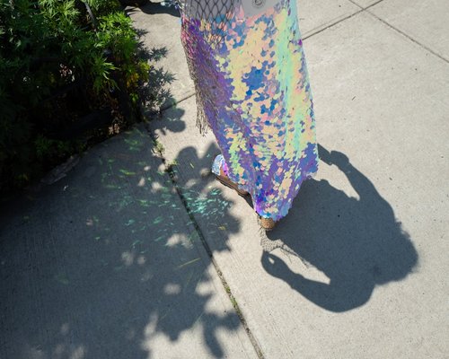 A person walking purposefully on a sunny sidewalk carrying a reusable grocery bag